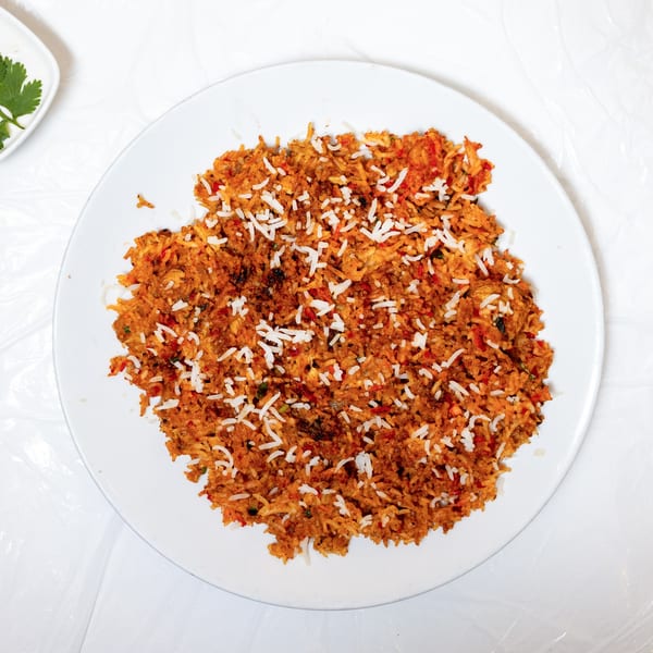 A white plate filled with orange-red biryani rice, topped with shredded white coconut.