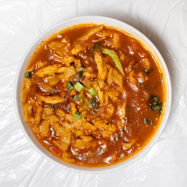 A white bowl filled with a rich, orange-red curry, chicken, and vegetables.