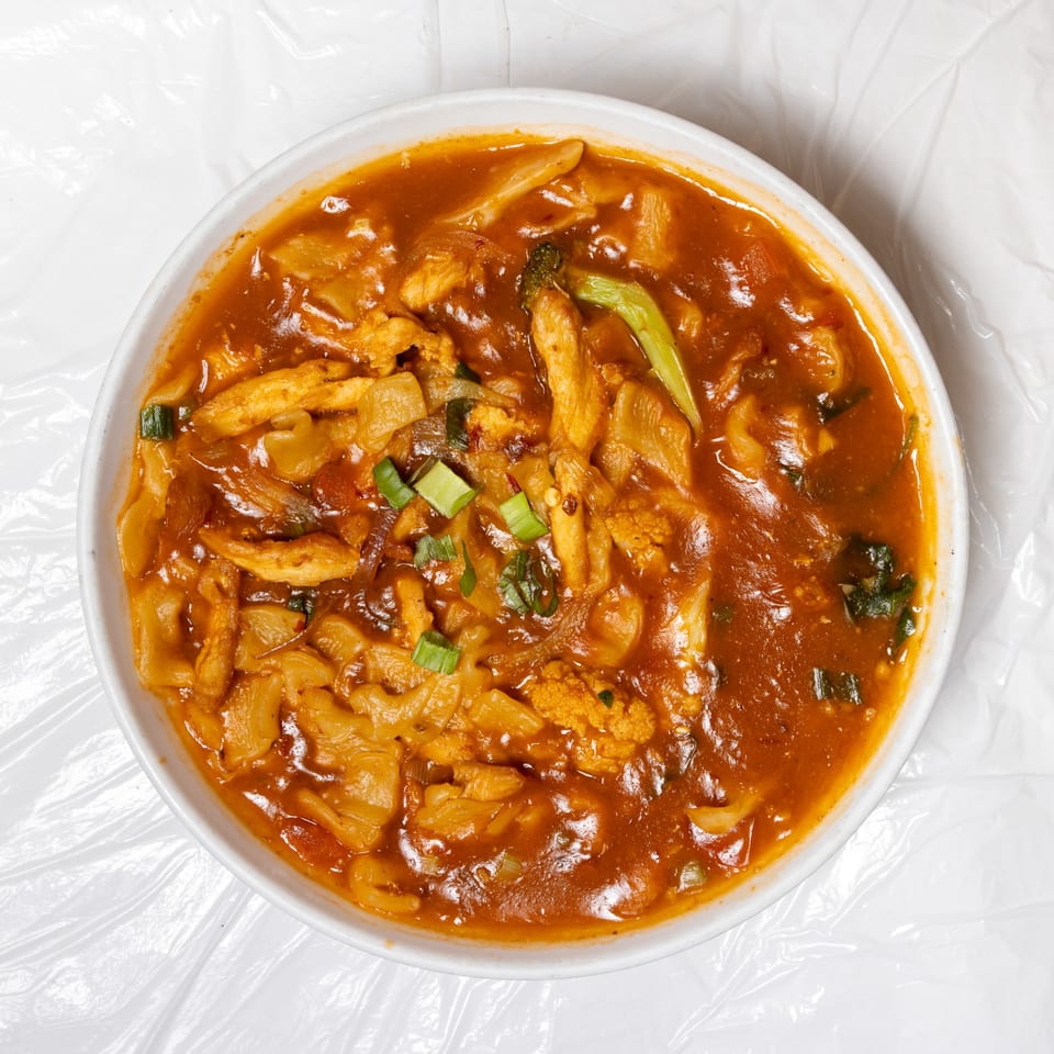A white bowl filled with a rich, orange-red curry, chicken, and vegetables.