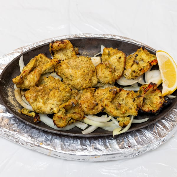 Sizzling chicken tikka with onions and a lemon wedge on a cast iron platter.
