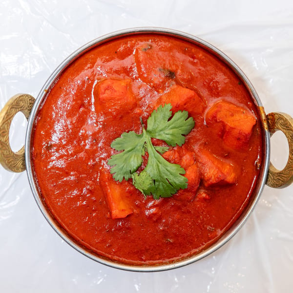 Top-down view of a brass bowl filled with vibrant red chicken tikka masala, garnished with cilantro.