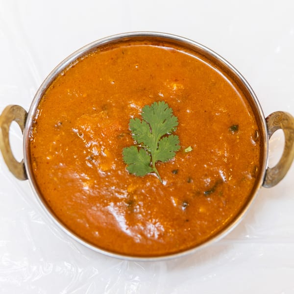 A metal bowl filled with orange curry, garnished with a fresh sprig of cilantro.