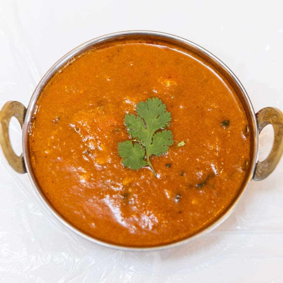 A metal bowl filled with orange curry, garnished with a fresh sprig of cilantro.