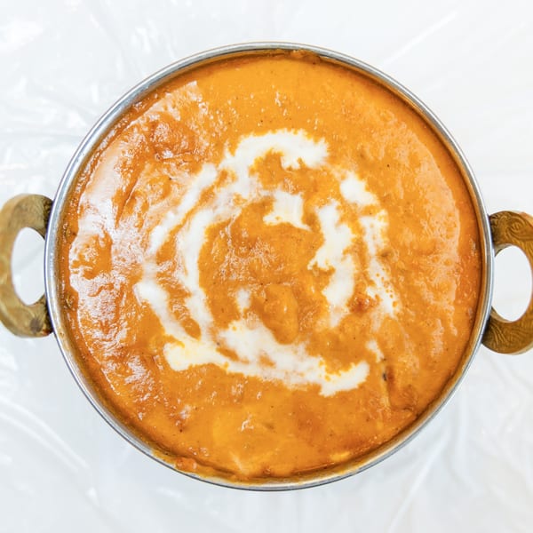 Overhead view of a metal bowl filled with orange curry, swirled with white cream.