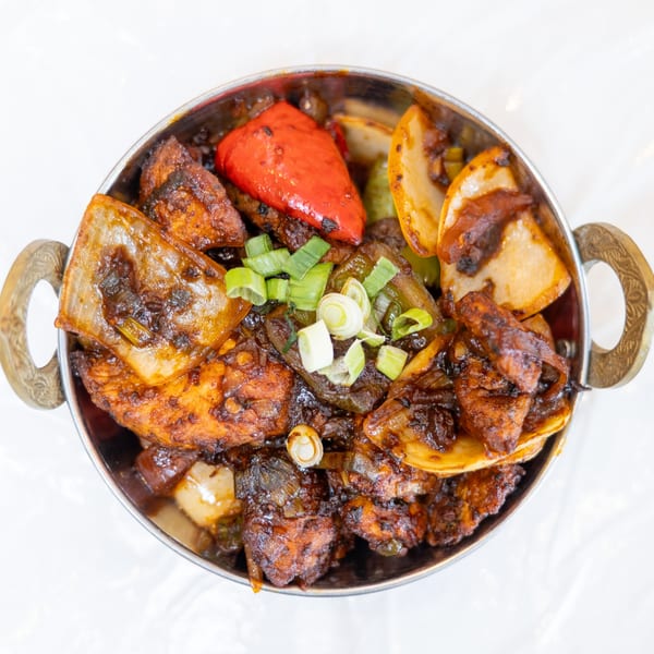Spicy chicken stir-fry with peppers, onions, and scallions in a metal bowl.
