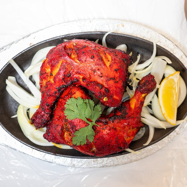 Two pieces of bright red tandoori chicken, garnished with cilantro, onions, and a lemon wedge.