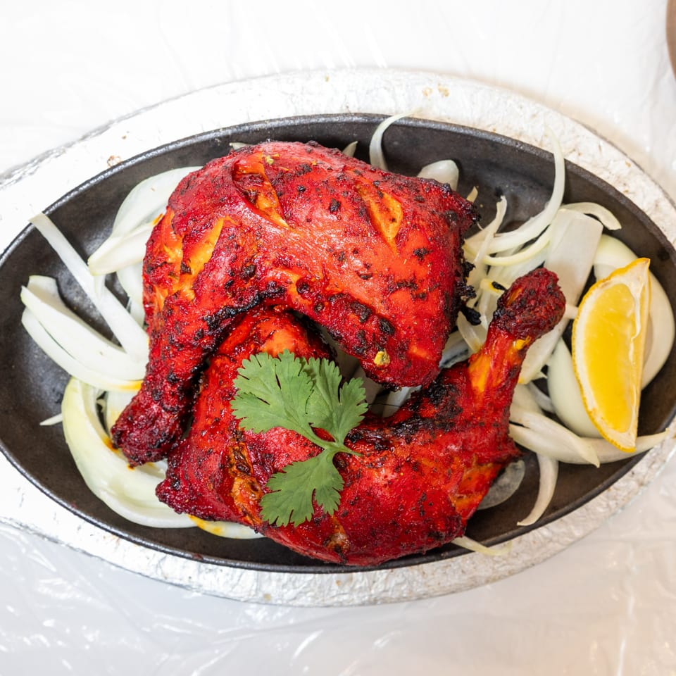 Two pieces of bright red tandoori chicken, garnished with cilantro, onions, and a lemon wedge.